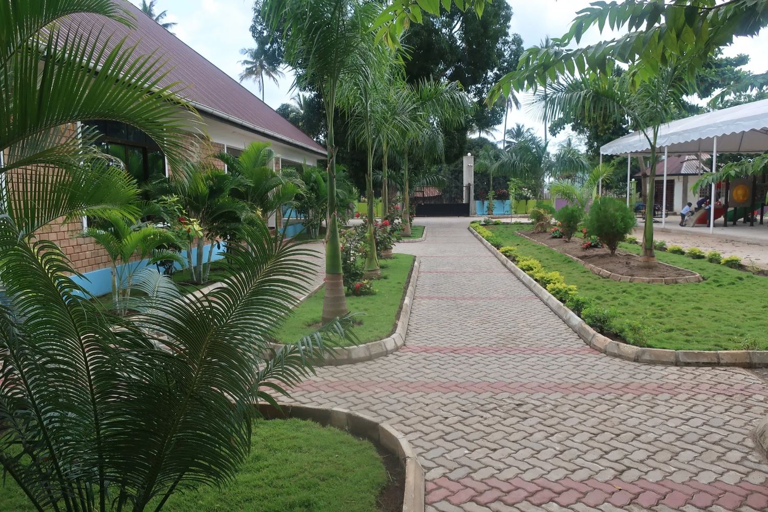 The early HBS campus in Kigamboni — palm-lined paths, low classroom blocks and gardens.